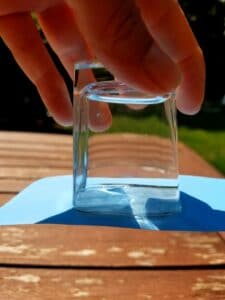 Science experiment with water and air showing glass is upside down full of water with only an index card covering the rim of the glass.