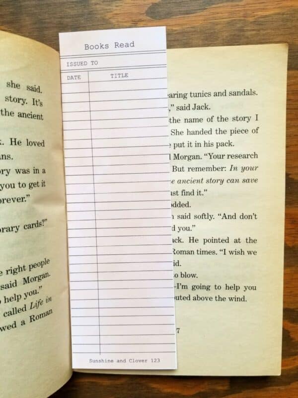 Library checkout card bookmark that can be used as a book log is shown in a paperback book.