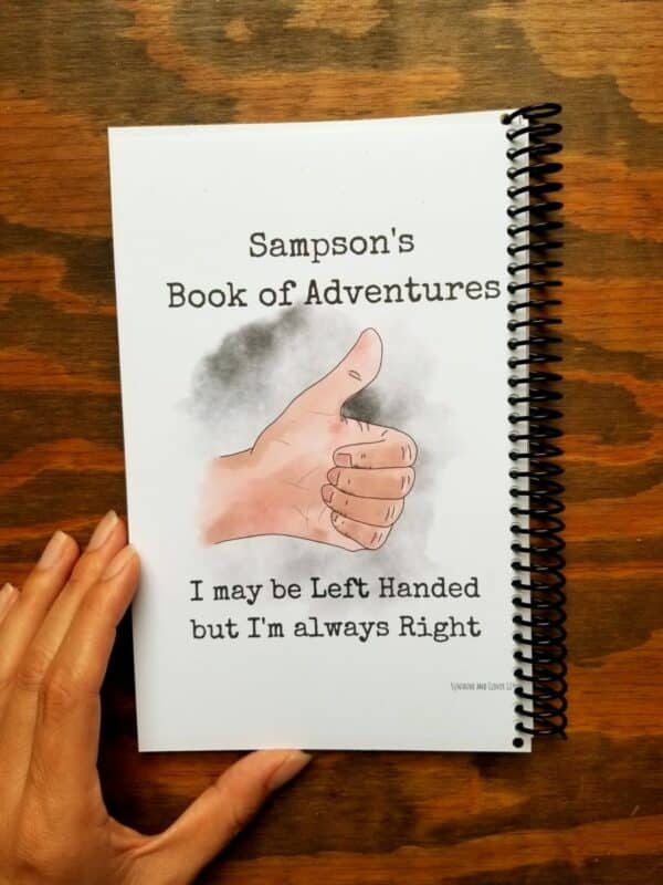 Customizable lefties notebook can be used as a journal, diary, book of poetry or sketchbook. This example shows being used as a book of adventures. Hand illustrated left handed thumbs up with customizable font and title.