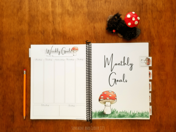 Homeschool planner shown with a weekly and monthly section. Homeschool planner comes spiral bound and has a red mushroom theme.