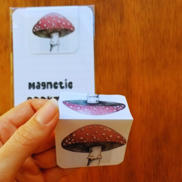 Bookmark is magnetic and features hand illustrated salmon colored mushroom with white spots.