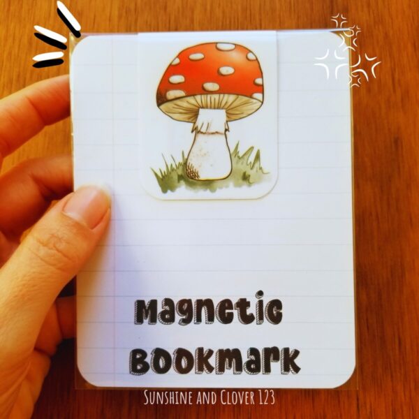 Magnetic bookmark with hand illustrated red mushroom and white spots on green grass.