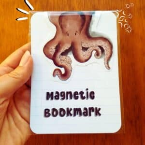 Octopus magnetic bookmark in clear bag sitting on a notebook paper. Octopus looks like its is hanging over the top of the page.